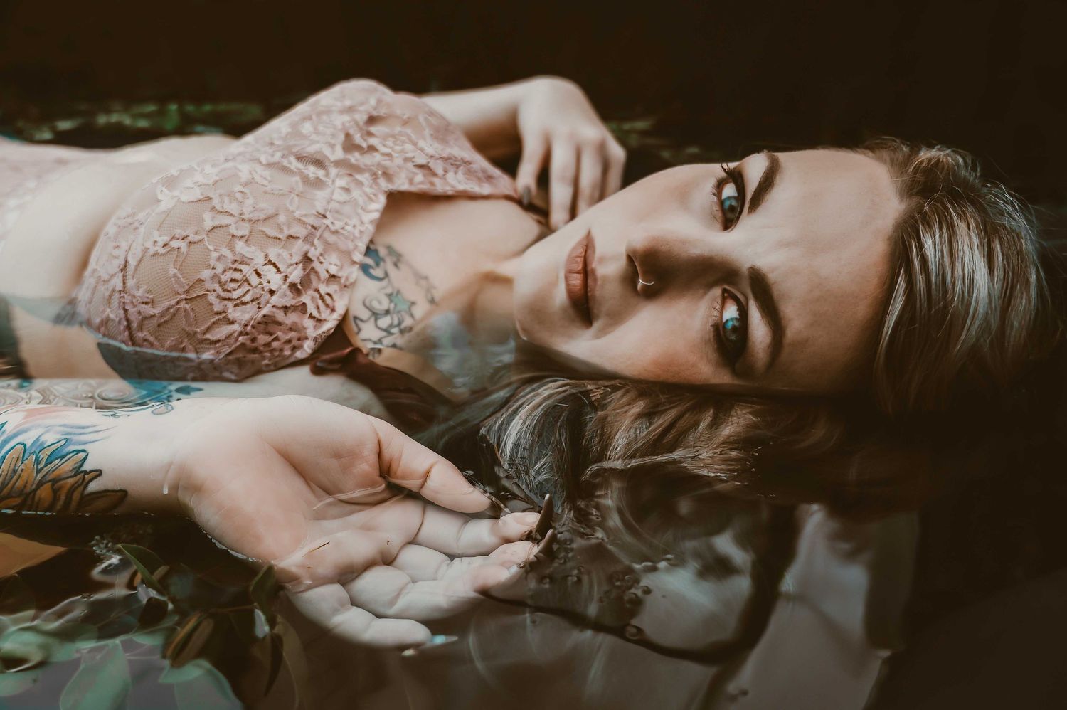 Boudoir portrait – woman in lace lingerie lying in water, powerful and captivating gaze.