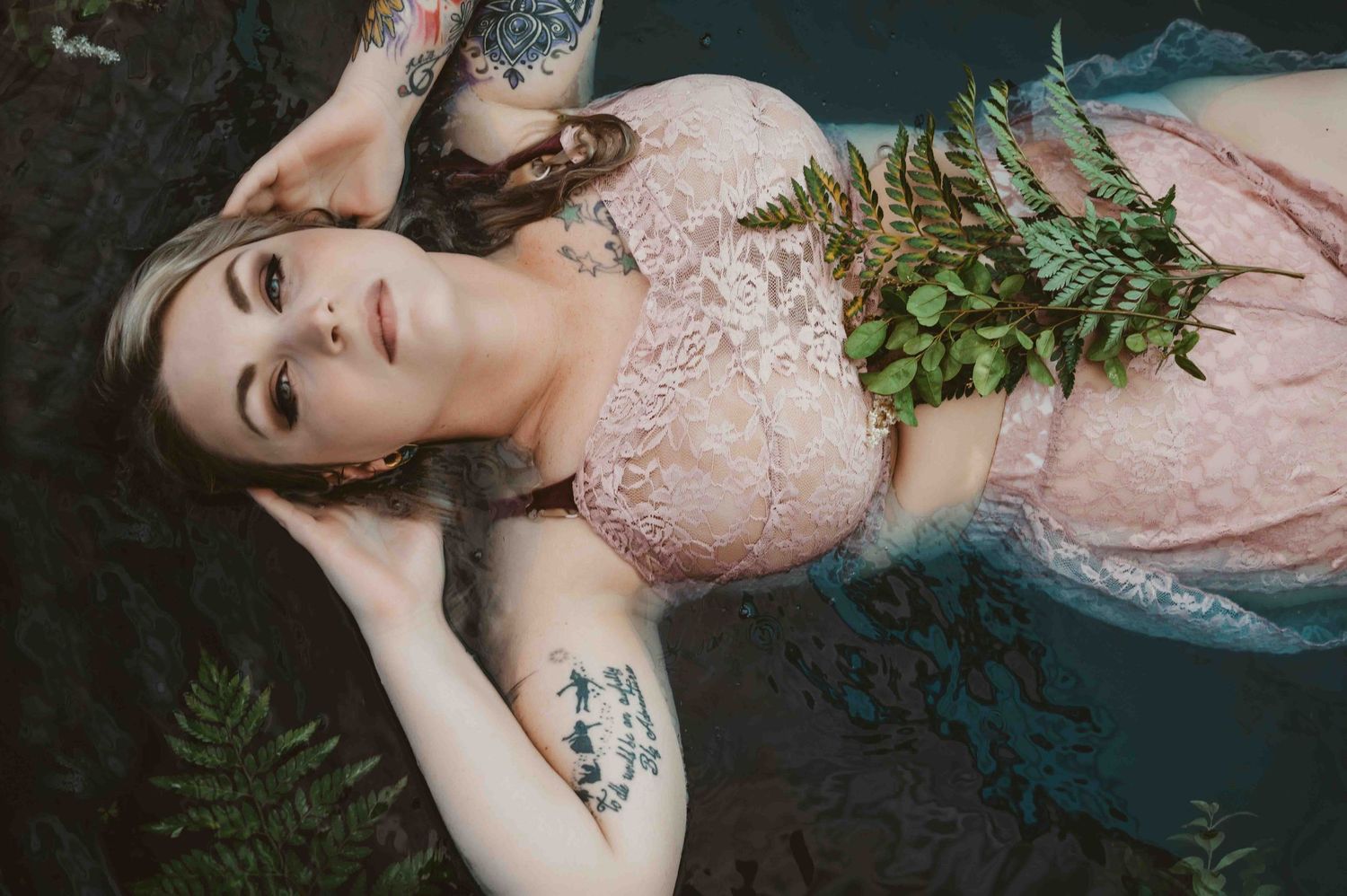 Ethereal boudoir photo – woman in pink lace lingerie floating in water with ferns, dreamy and serene.