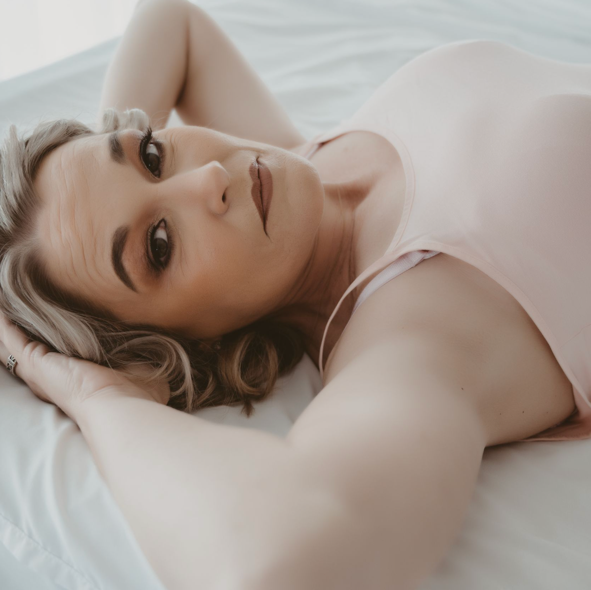 boudoir photograph of woman in Ashland, KY with pink shirt on bed
