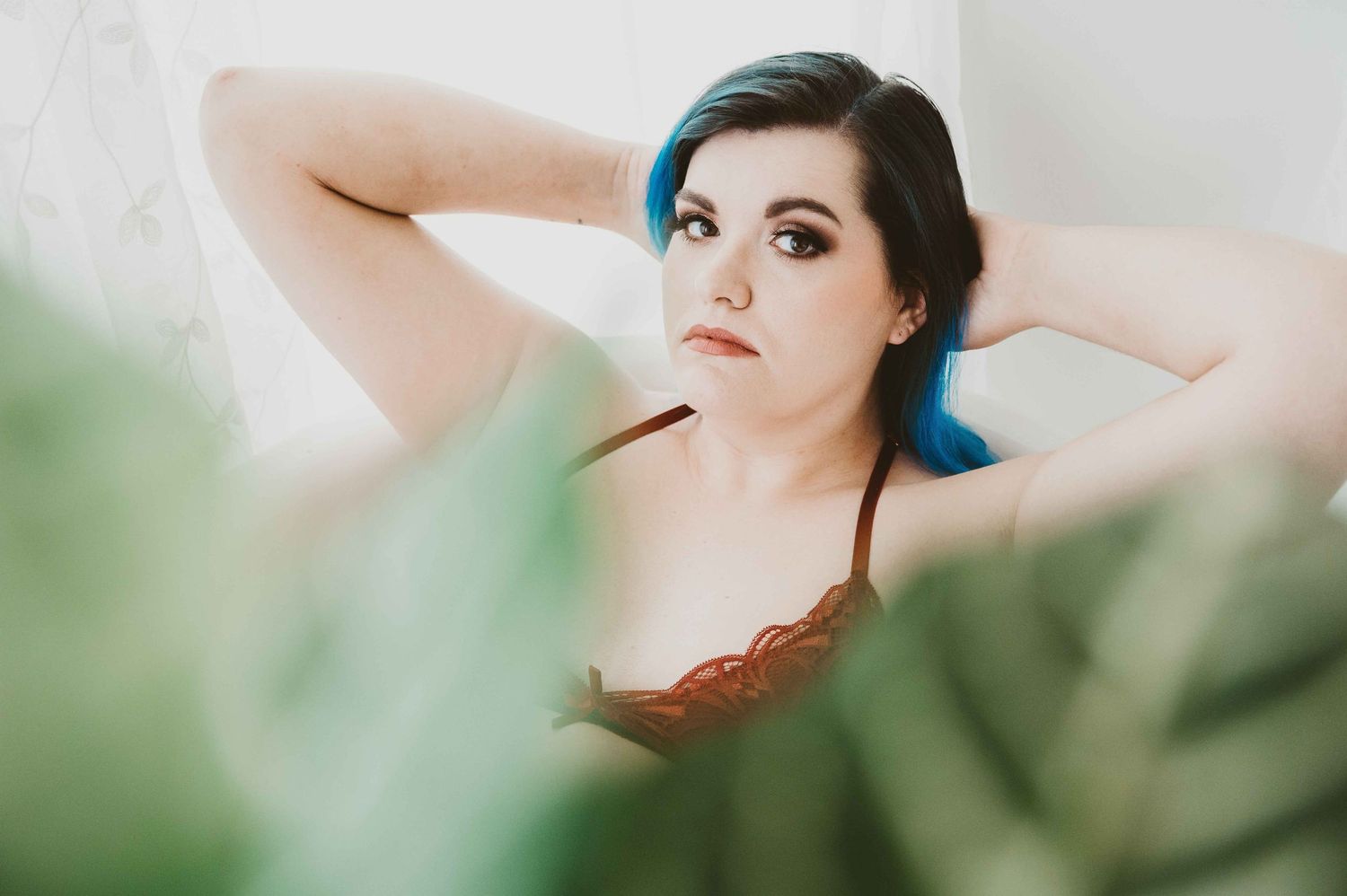 Boudoir photography – woman with blue hair in red lingerie, natural light and soft greenery.