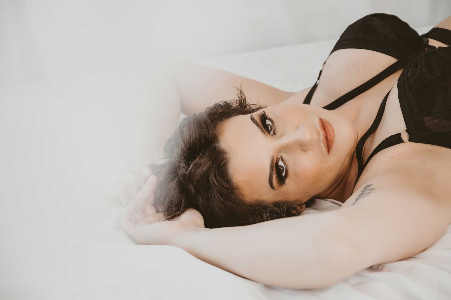 Empowering boudoir photo – woman reclining on bed in black lingerie, confident expression.