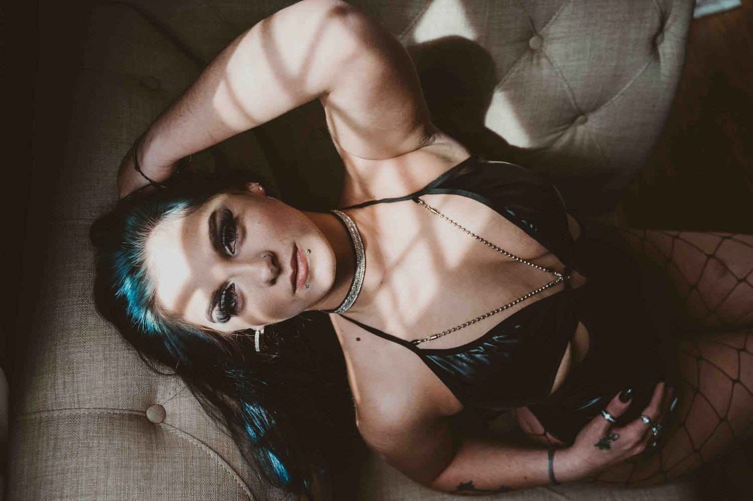 Woman in black lingerie and jewelry reclining on a tufted chair with dramatic light.