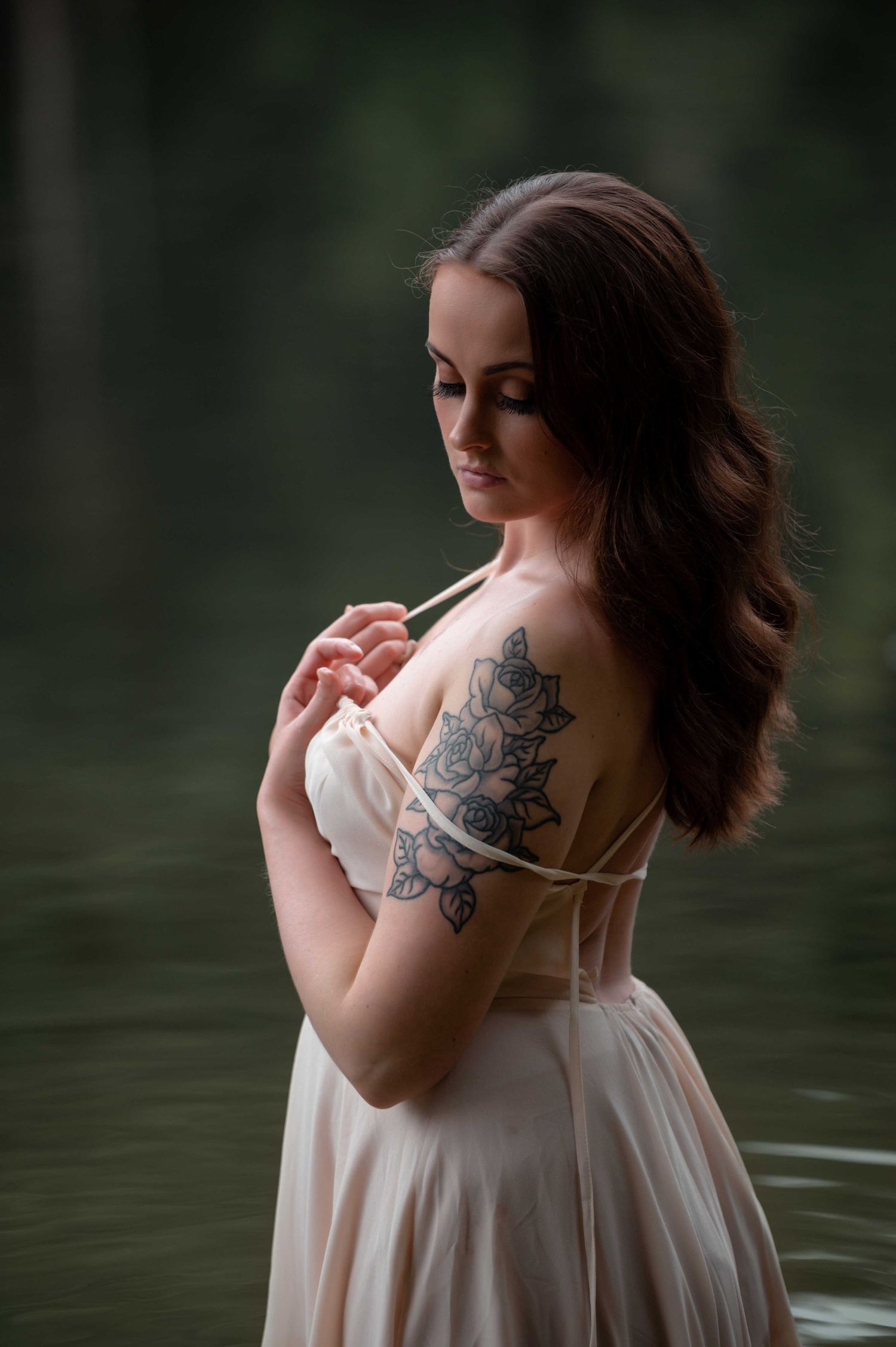 Outdoor boudoir session – woman in flowing dress by lake, soft and reflective pose.
