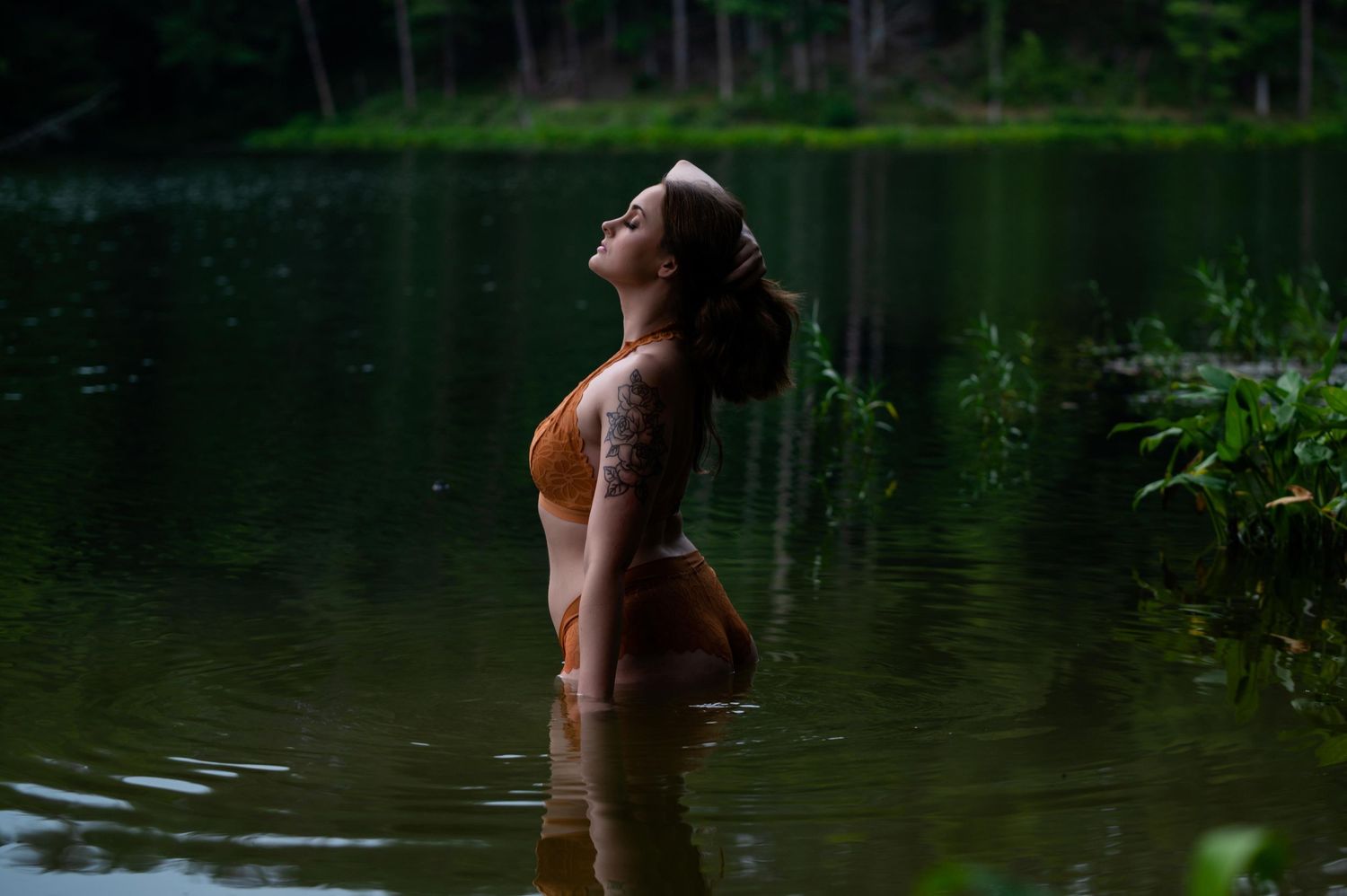 Woman in burnt-orange lingerie stands in a forest lake, Kentucky boudoir photography capturing body confidence outdoors.
