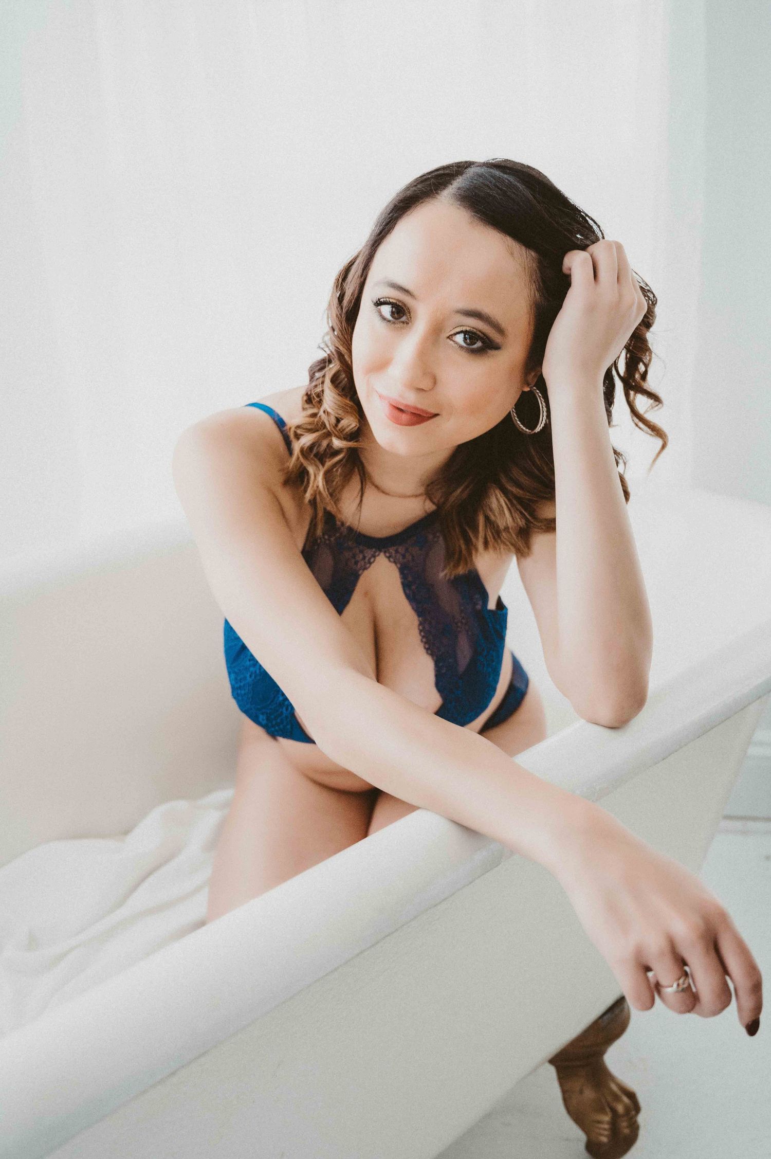 Boudoir photo – woman in blue lace lingerie in vintage tub, relaxed and radiant.