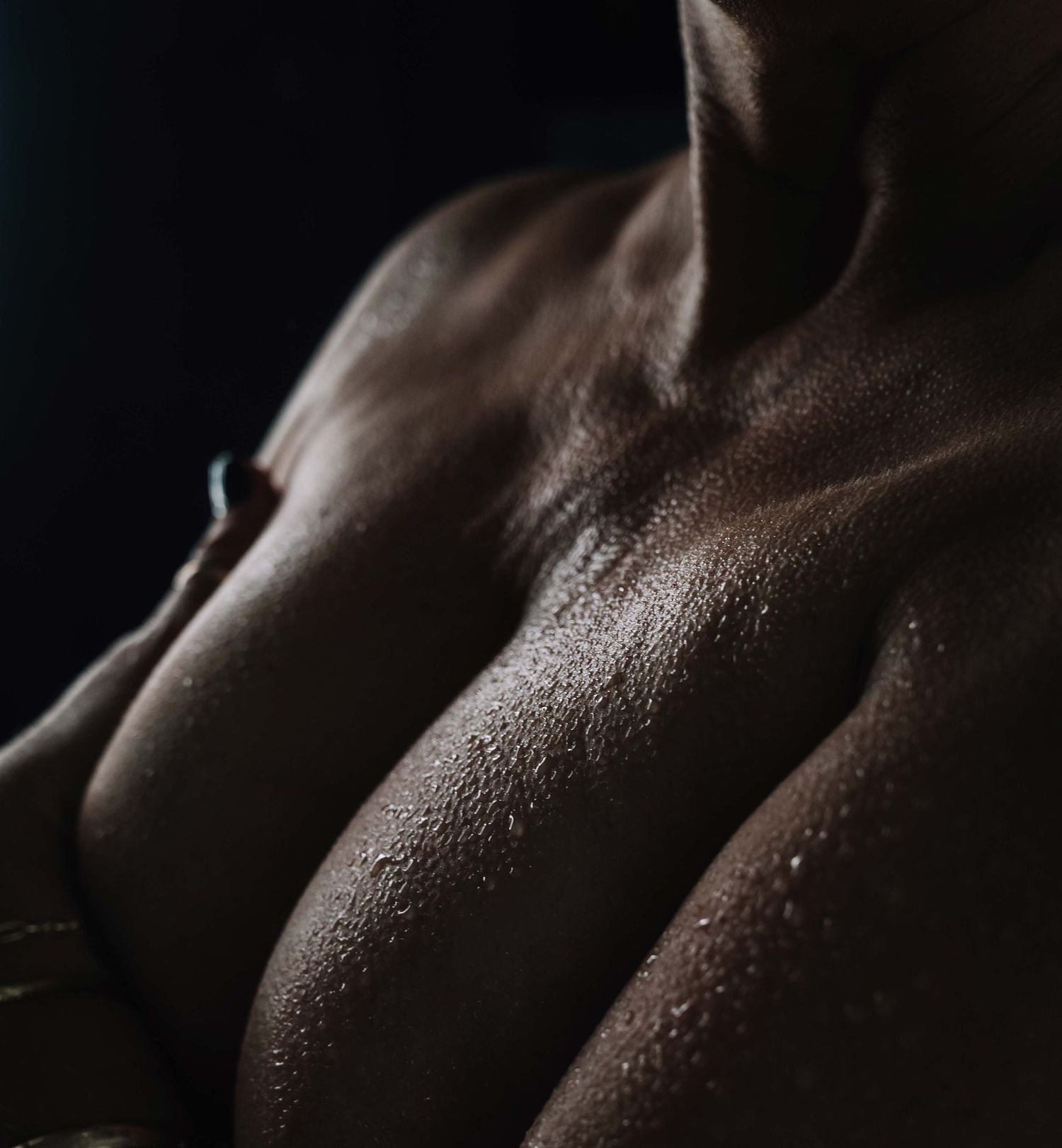 Artistic boudoir close-up with water droplets on skin, dramatic and powerful.