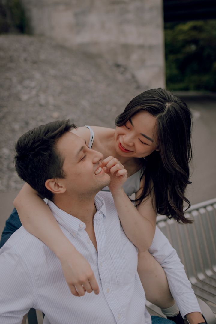 Narrative Couple Portraits - She leans over his shoulder and touches his face, smiling lovingly.