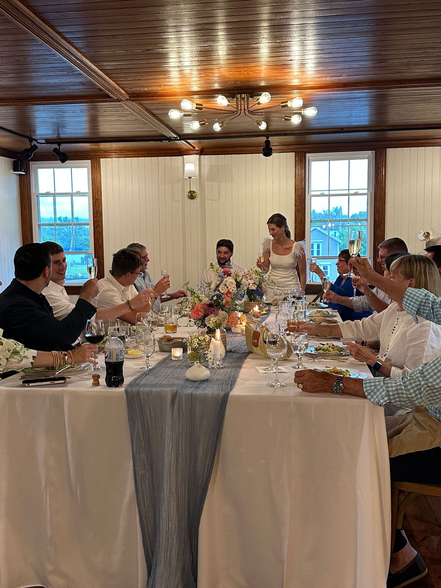 Wedding guests raising glasses in a toast at elegantly set rehearsal dinner table in rustic venue.