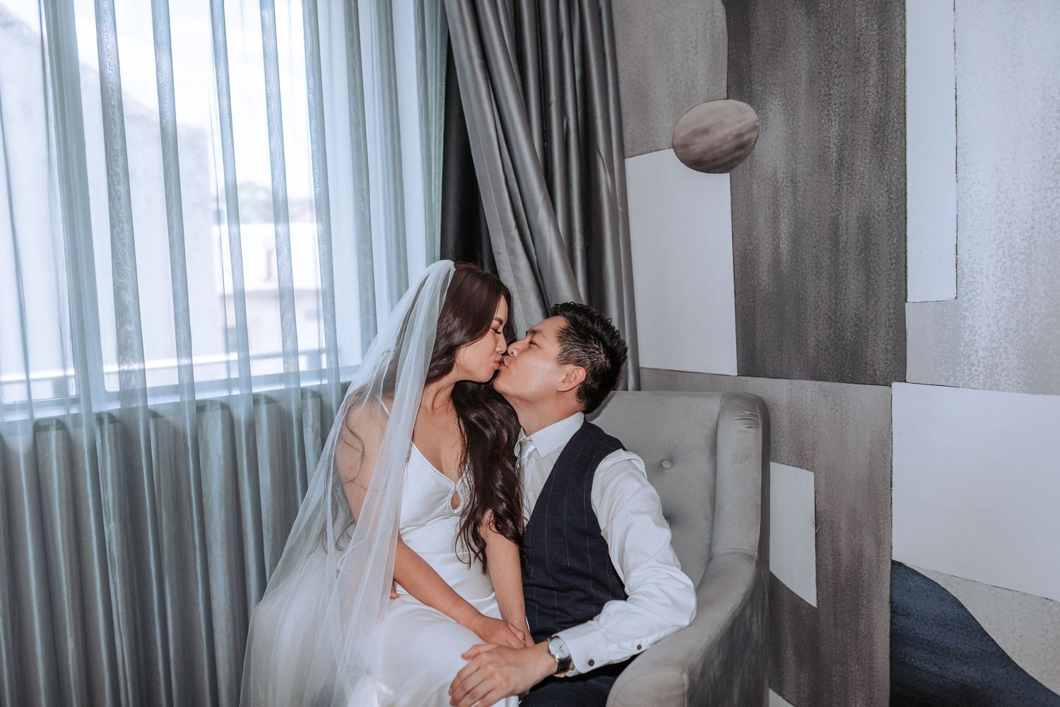 A bride and groom share a romantic kiss while a football spirals through the air above them in a modern room.