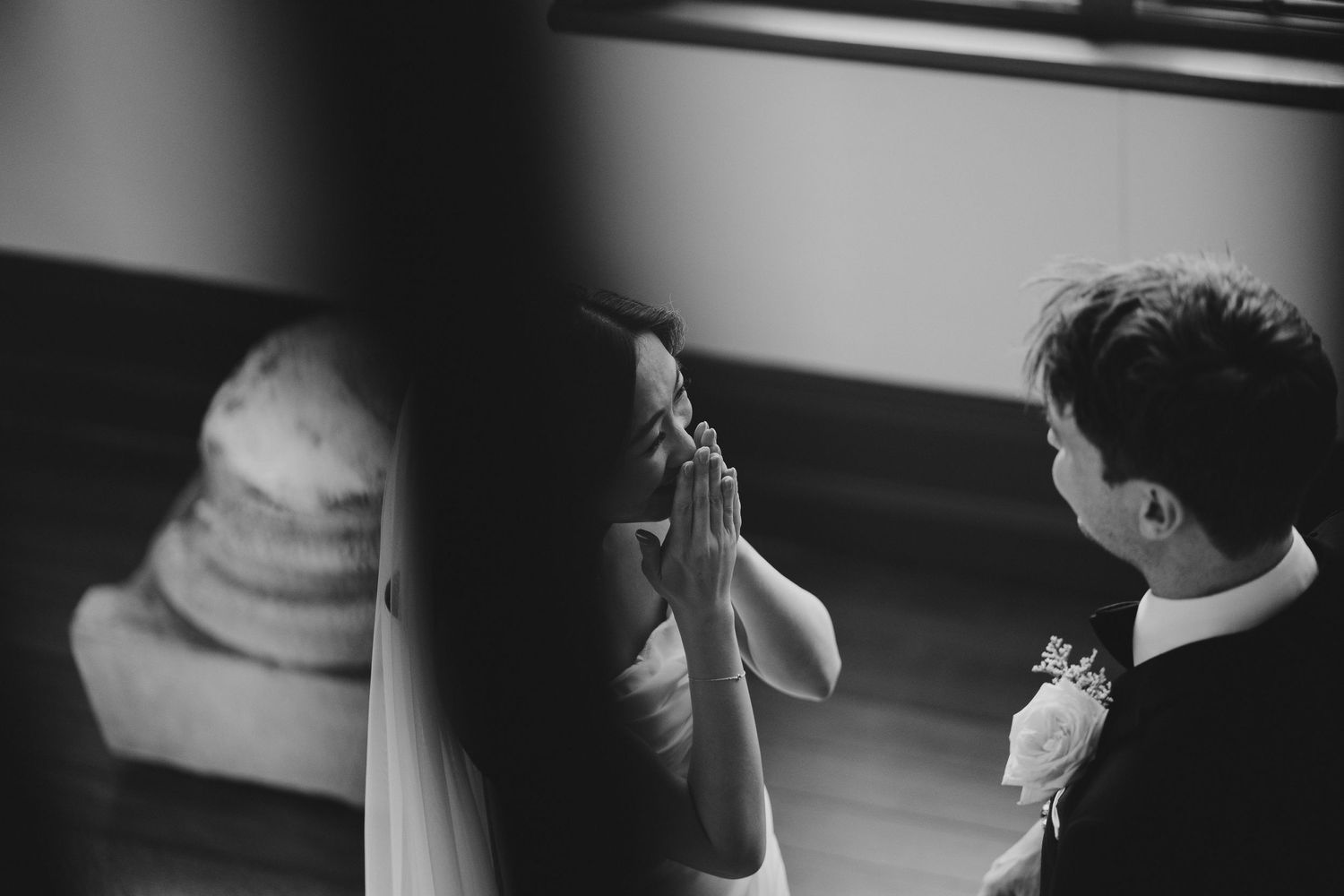 A black and white photograph captures an intimate moment between a bride and groom during their wedding ceremony.