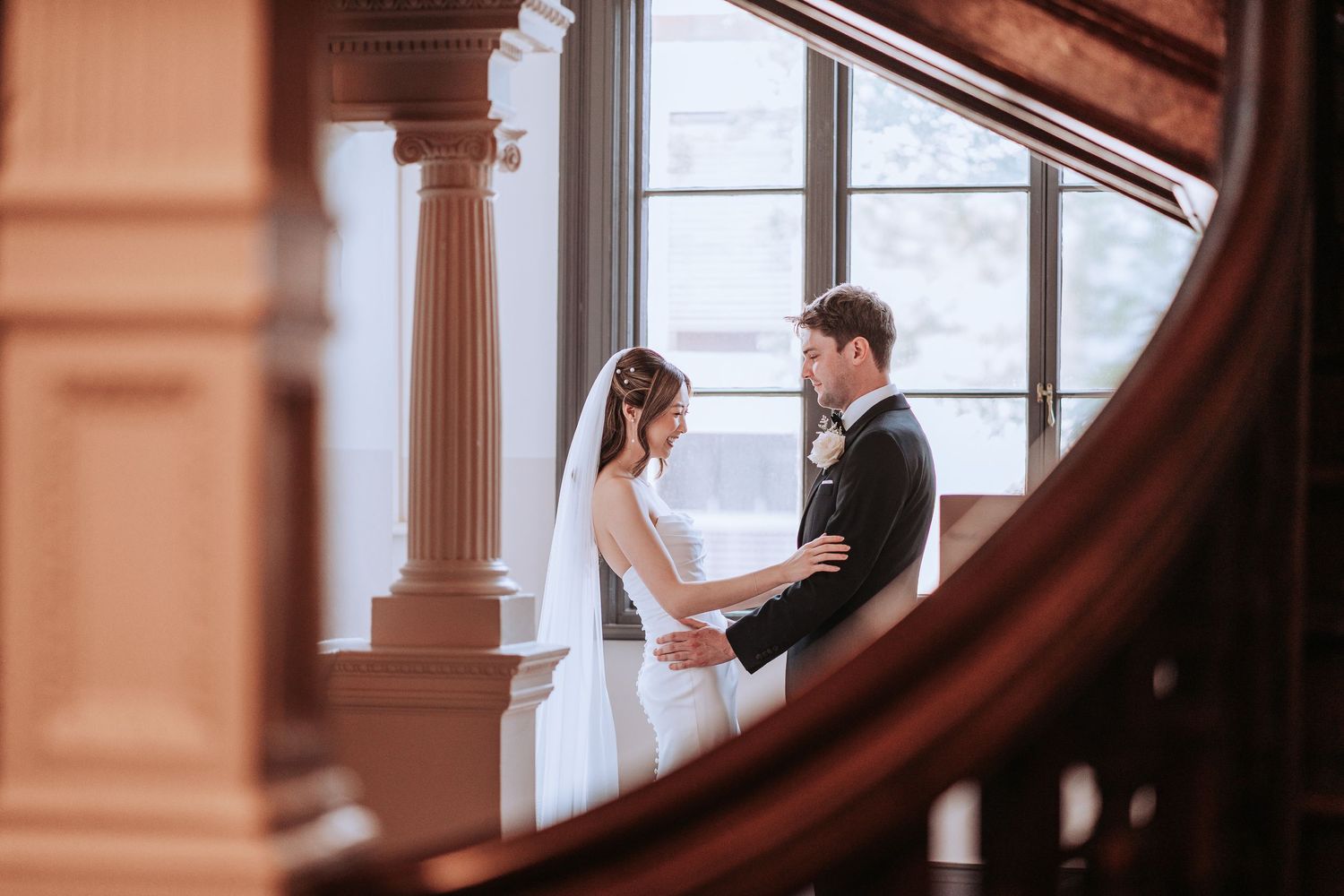 Couple in wedding attire standing in front of ornate architectural columns and woodwork.