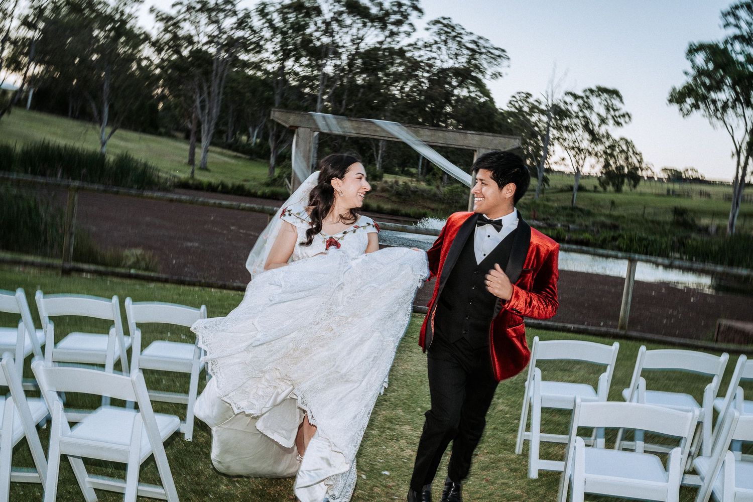 A romantic outdoor wedding ceremony setup with white folding chairs arranged on a grassy lawn at sunset.