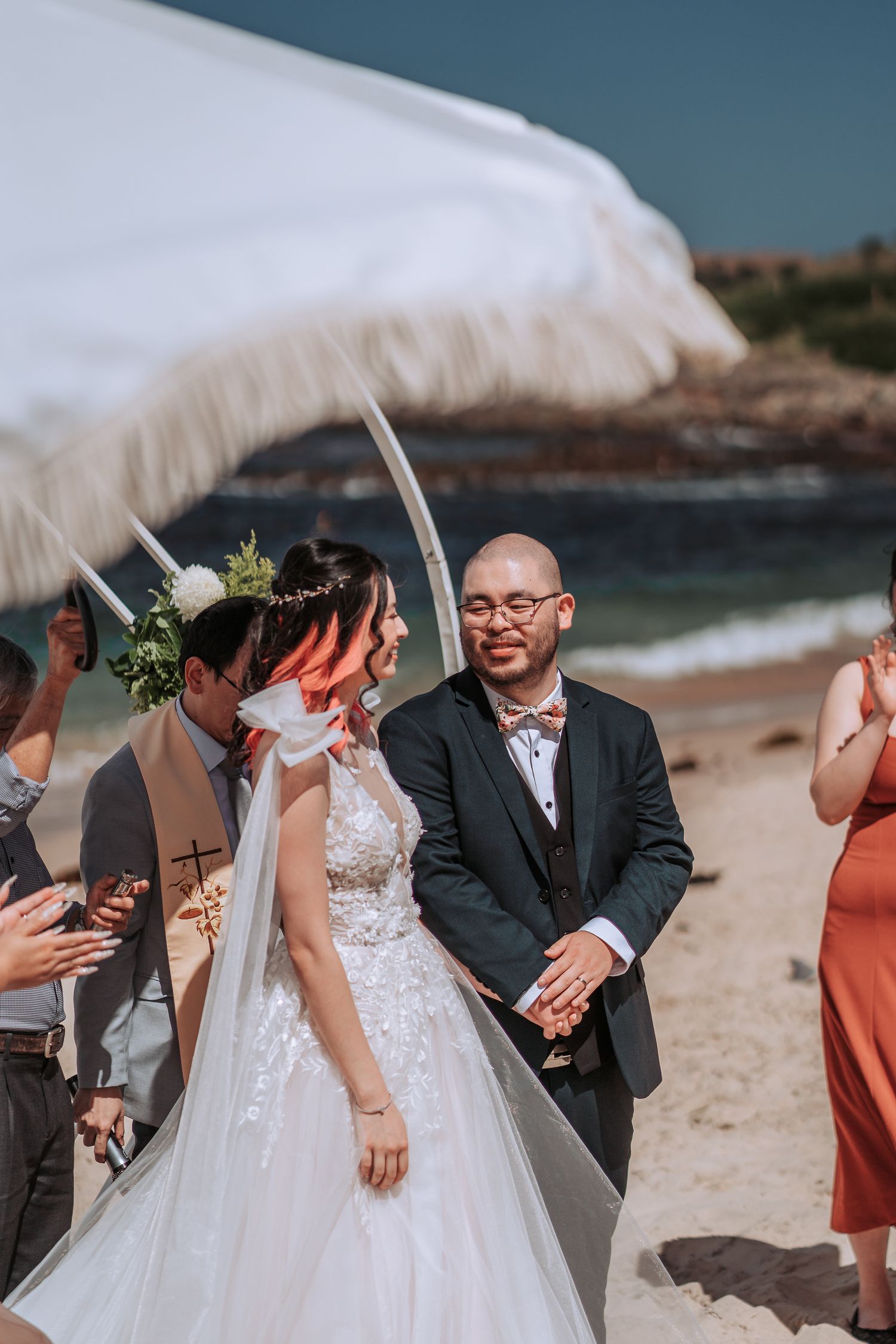 A beachside wedding ceremony with a white fabric canopy blowing in the wind.