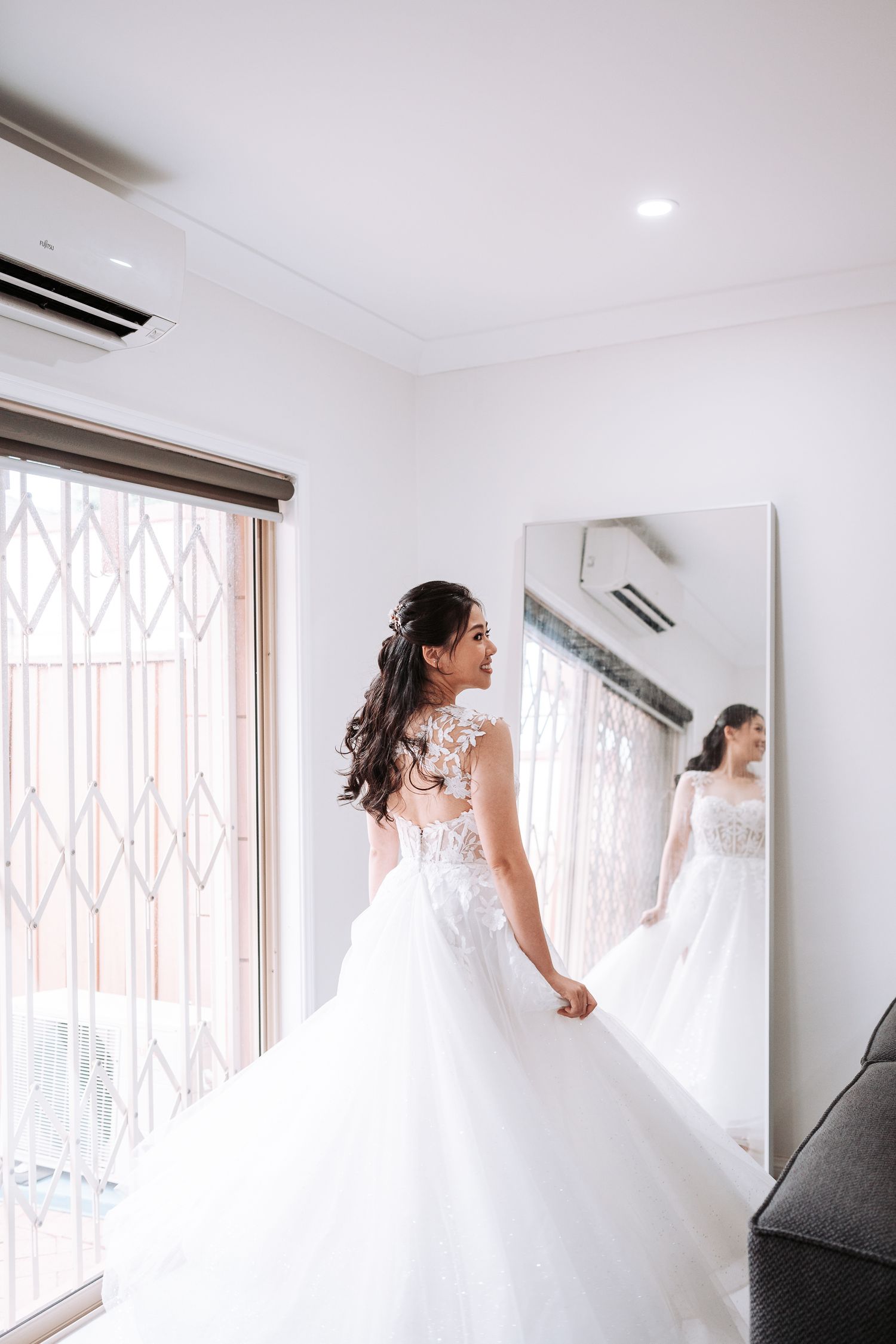 A person wearing a white wedding gown standing in a bright indoor space with geometric window patterns.