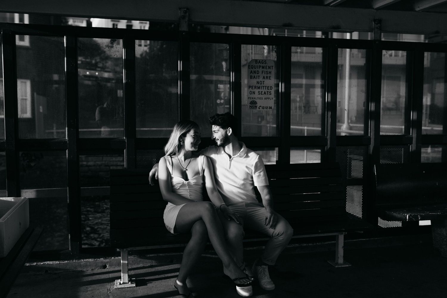 A couple sits intimately together in a dark bar or lounge setting captured in black and white photography.