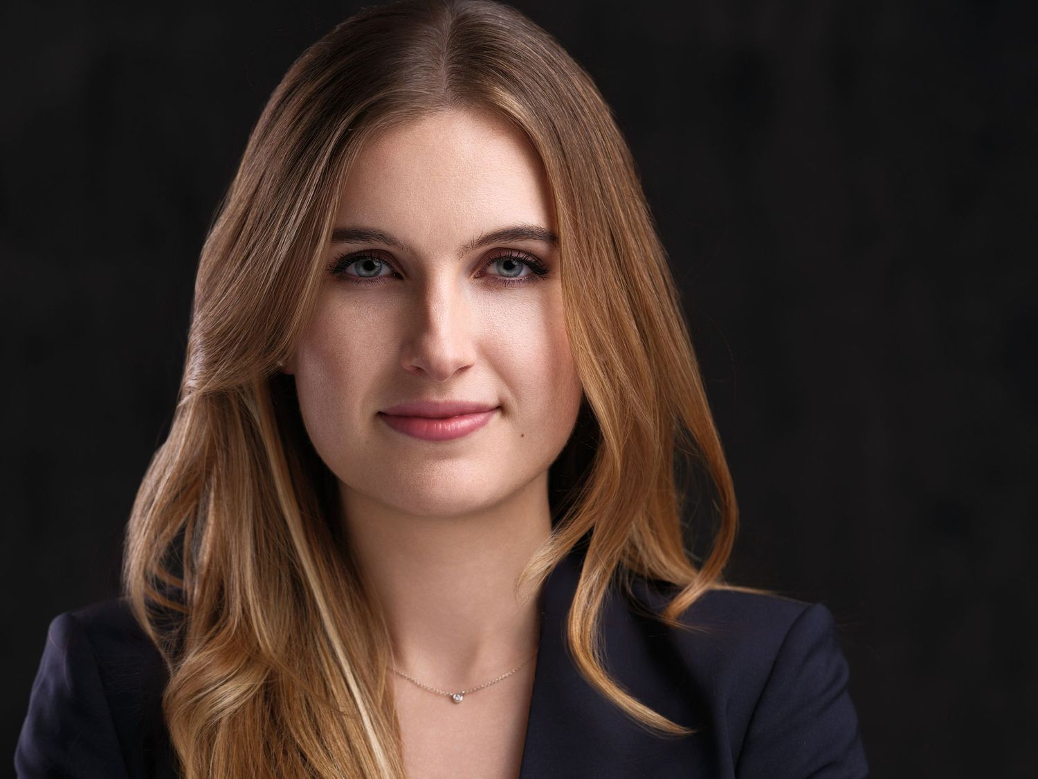 Professional headshot portrait of someone wearing a navy blazer with soft lighting against a dark background.