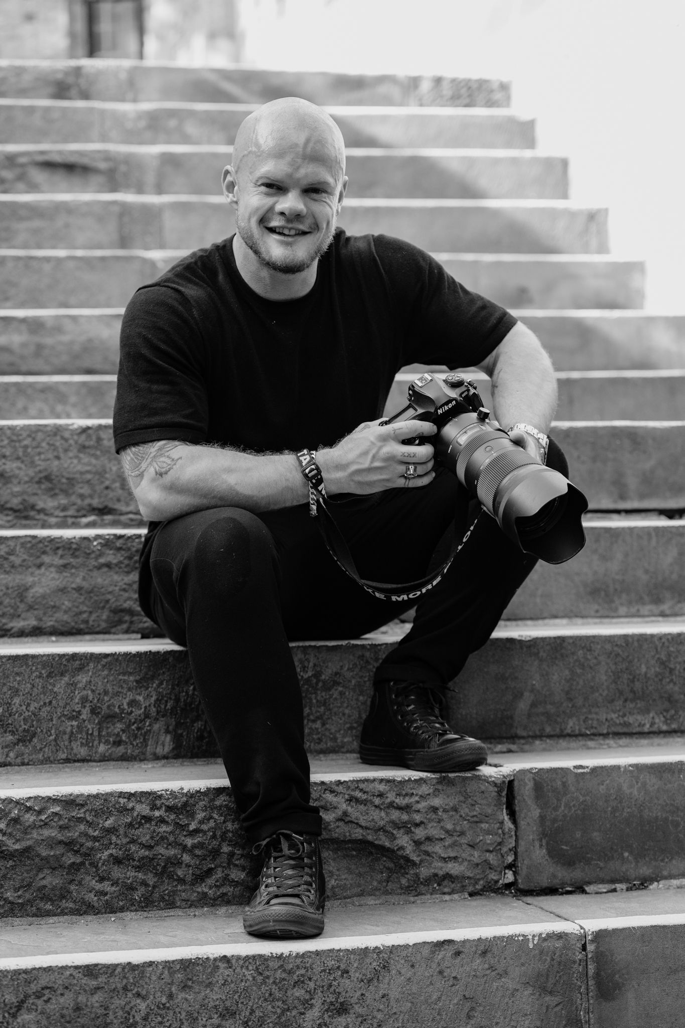 Professional photographer with camera equipment sitting on stone steps outdoors.