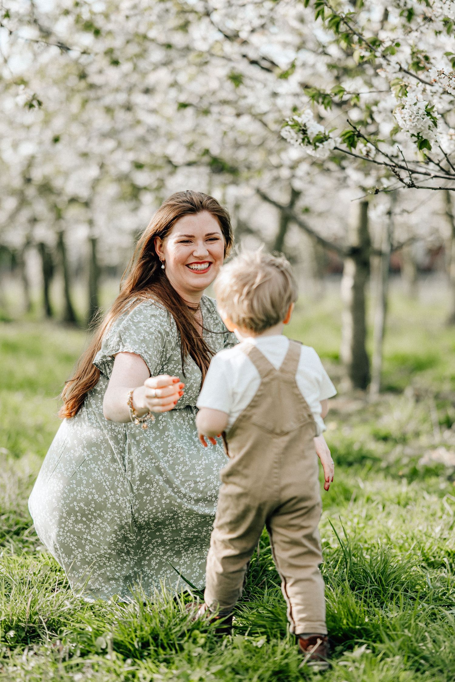Mother and toddler share a joyful moment together among blooming spring cherry trees in a sunlit orchard.