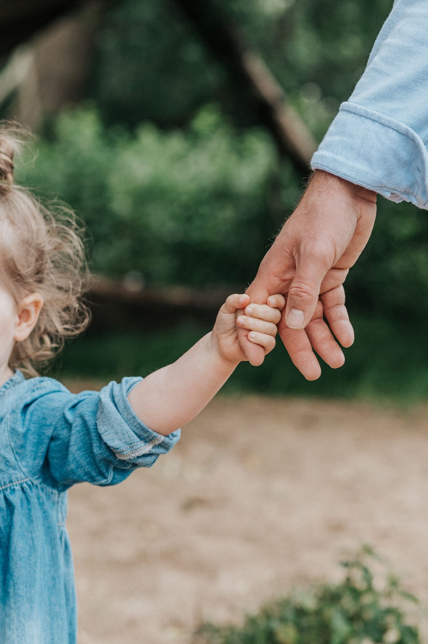 A close-up of small hand holding an adult's hand in a tender outdoor moment.