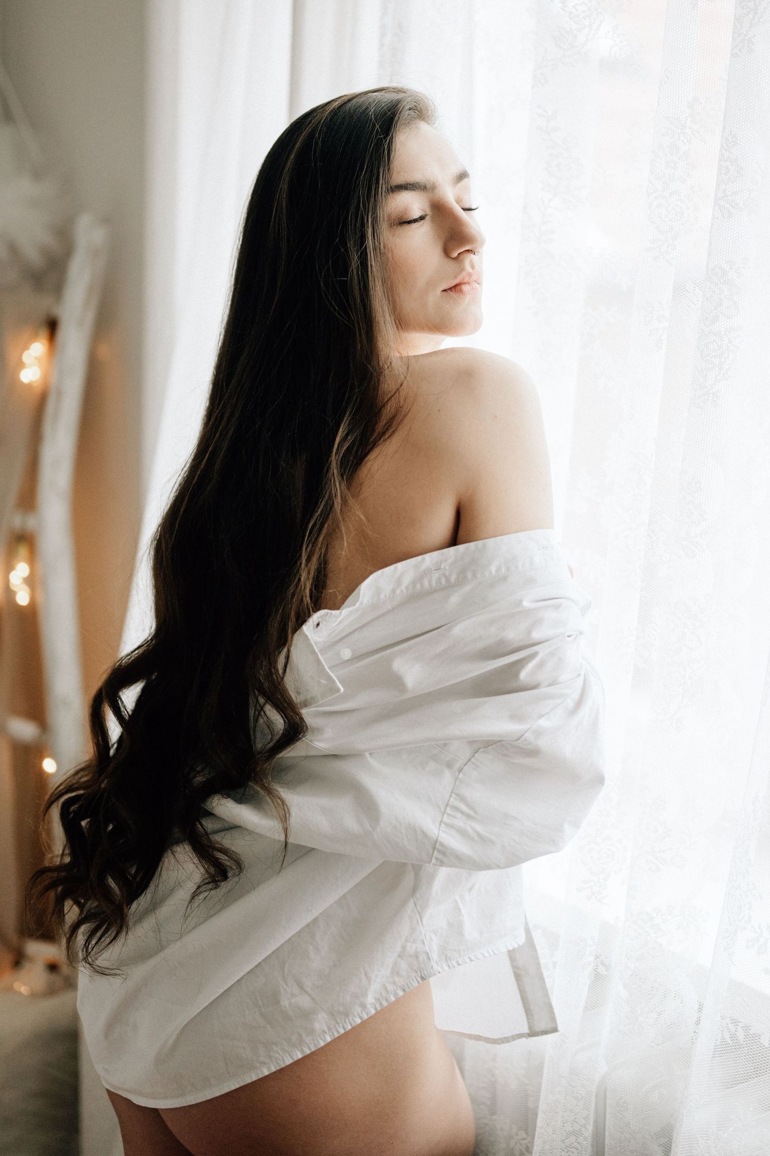 A series of four boudoir photos showing a woman in white fabric near a window with soft natural lighting.