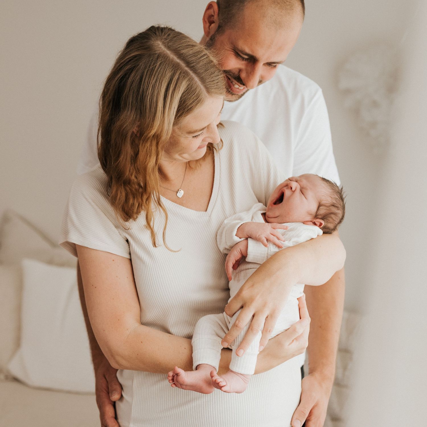 Parents gazing lovingly at their newborn baby in a serene white room.