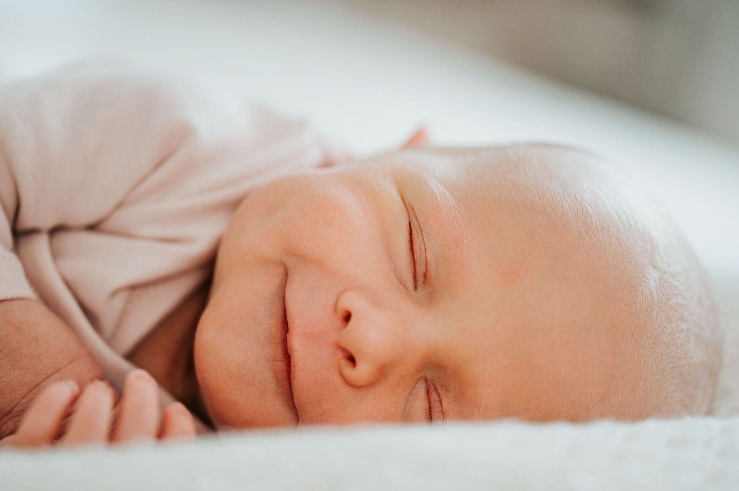 Peaceful sleeping newborn baby with rosy cheeks against soft white bedding.