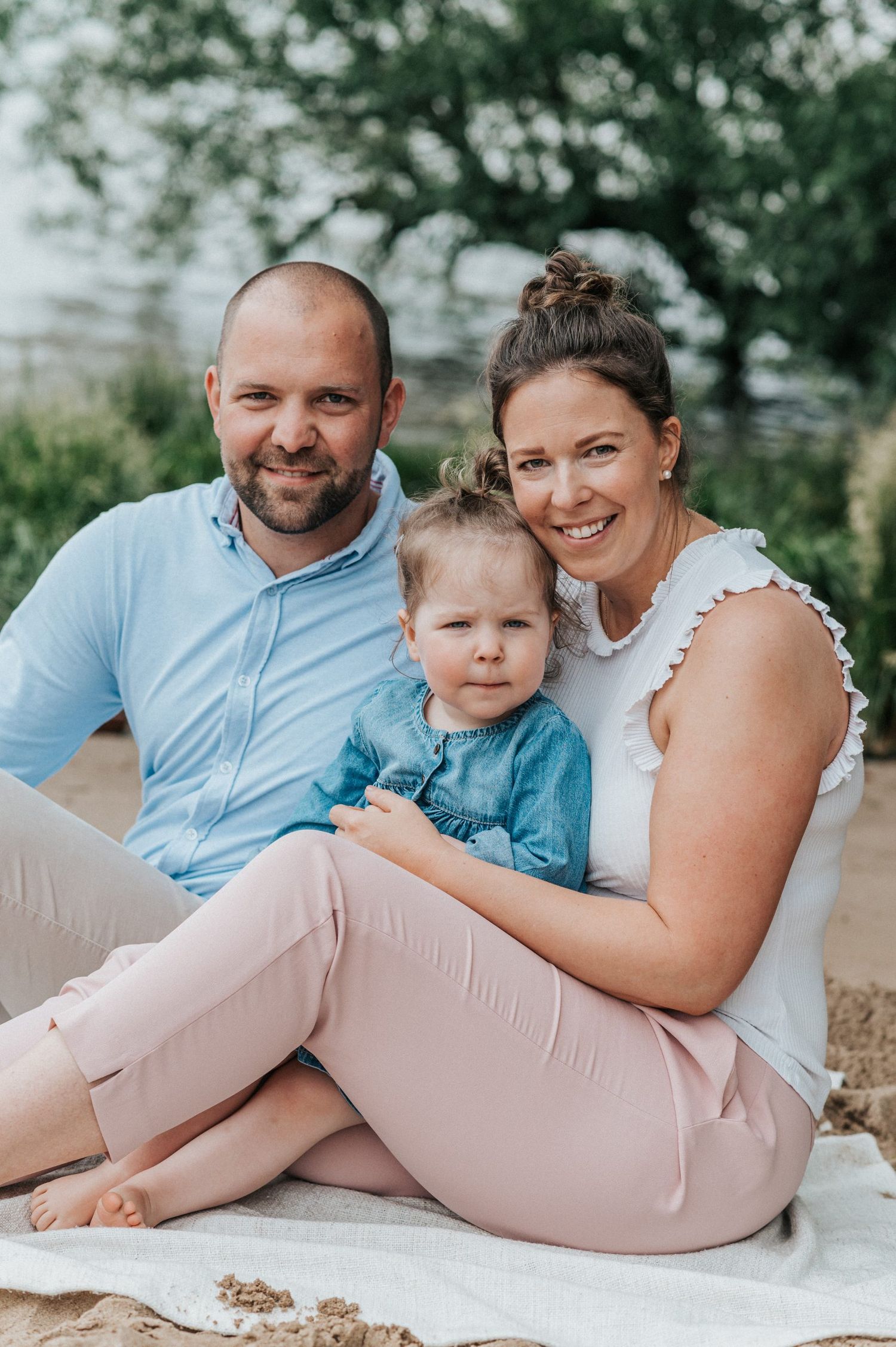 Family of three poses together on blanket during outdoor summer photoshoot.