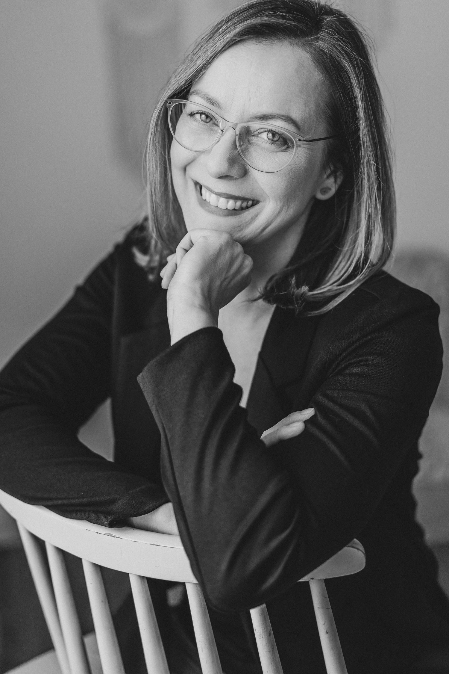 Professional headshot of someone in glasses and black sweater smiling warmly.