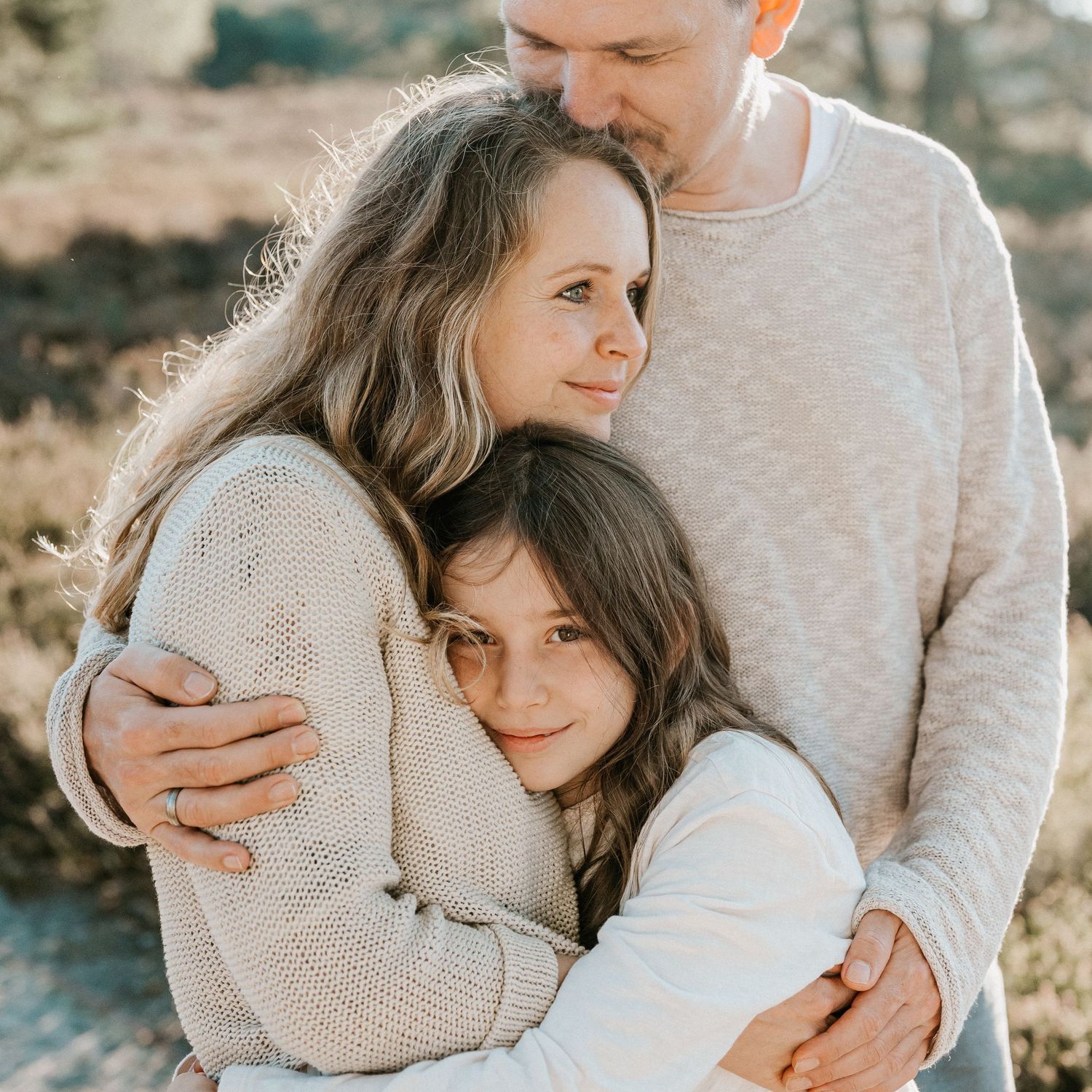 Close up portrait of family members embracing outdoors in soft natural lighting wearing cozy sweaters.