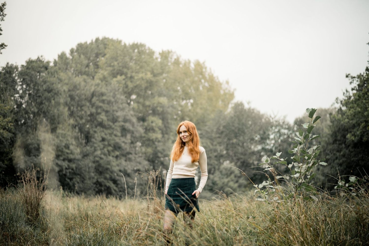 Atmospheric portrait of a lone figure standing in a misty summer meadow at golden hour.