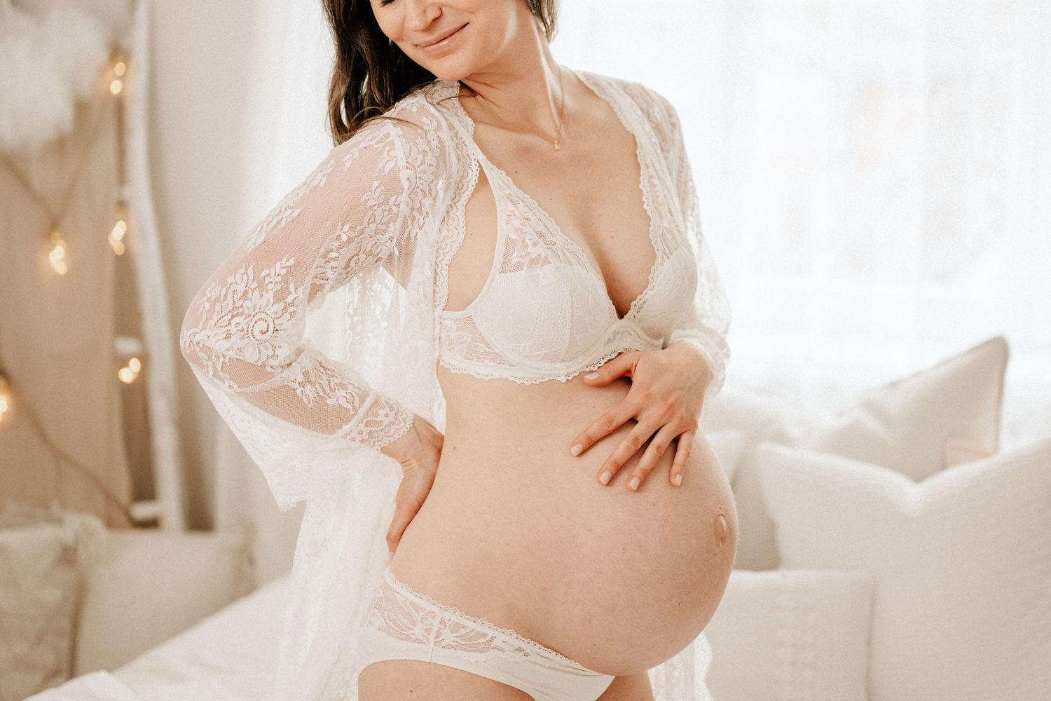 Intimate maternity portrait with white lace and string lights in background.