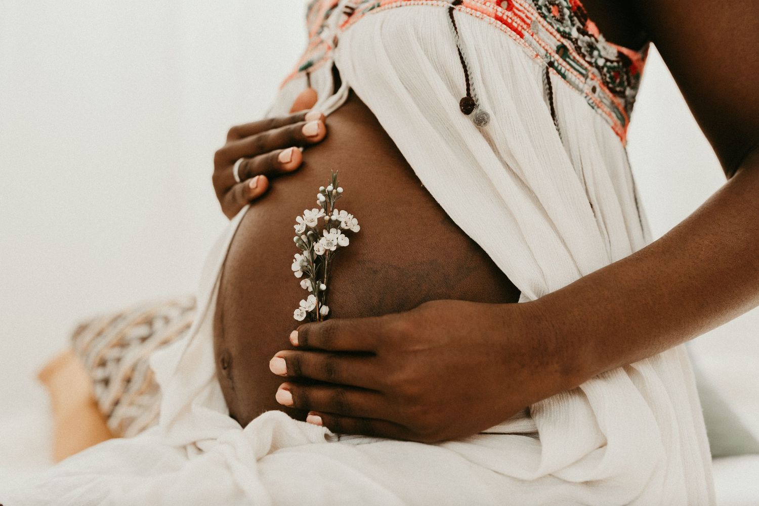 Close-up of hands gently resting on pregnant belly in white dress.