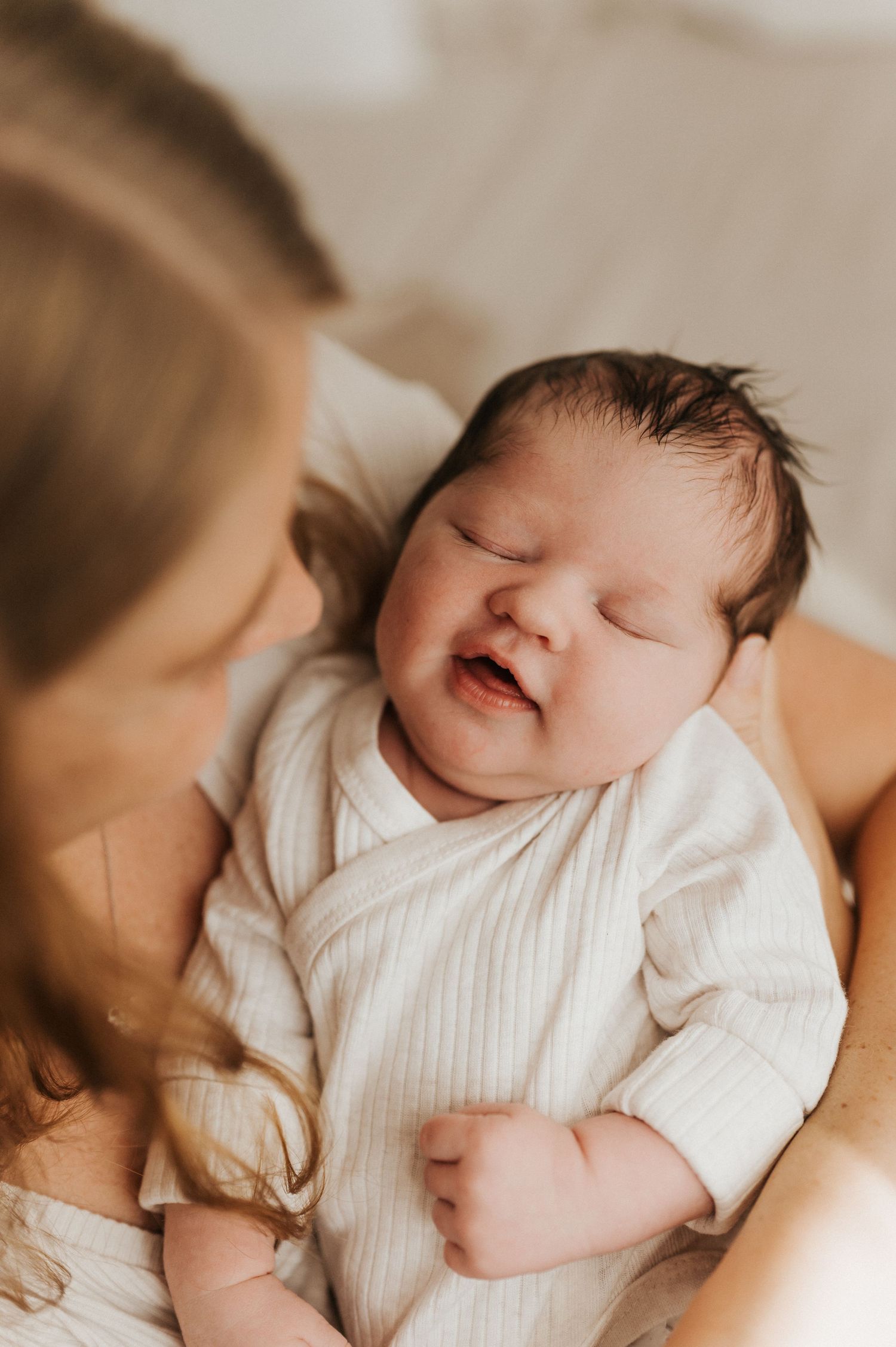 Newborn baby in white outfit smiling while sleeping peacefully.