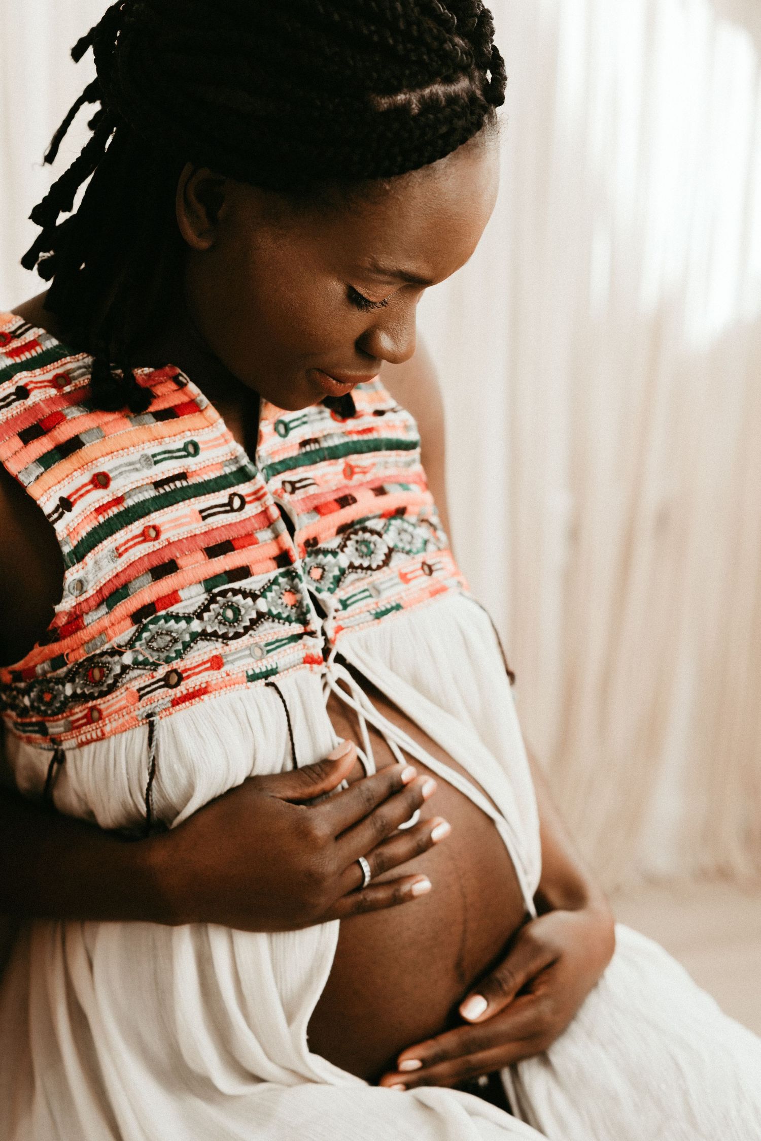Expecting mother in coral patterned top holds belly in bright sunlit room.