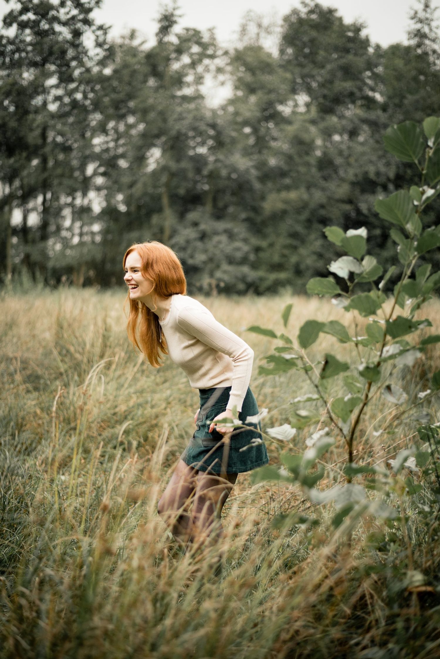 Whimsical outdoor portrait in tall grass with natural backlighting and forest scenery.