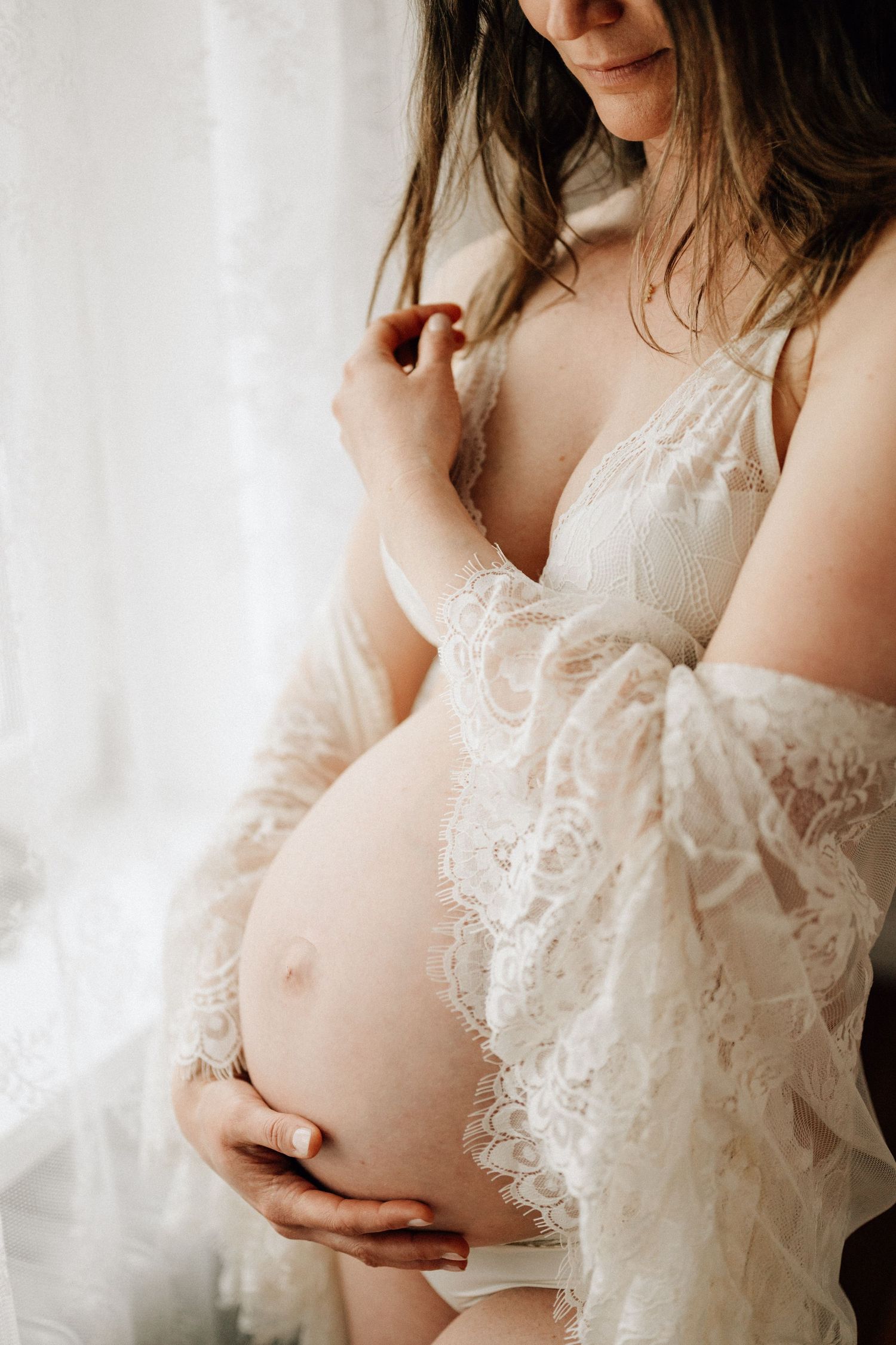 Artistic maternity photo featuring delicate lace dress and baby bump silhouette.