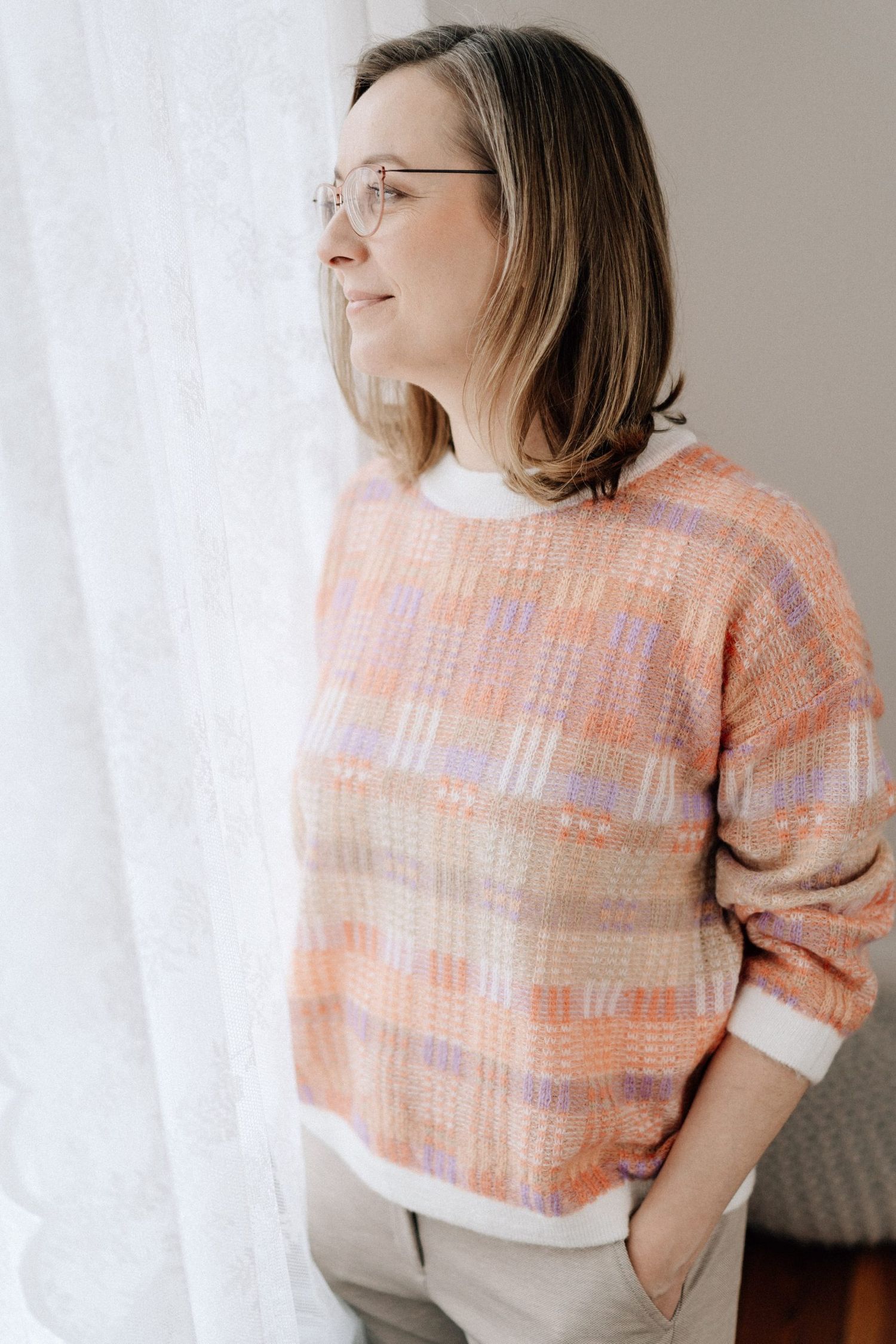 Fashion series featuring peach plaid sweater and glasses in minimalist indoor setting.