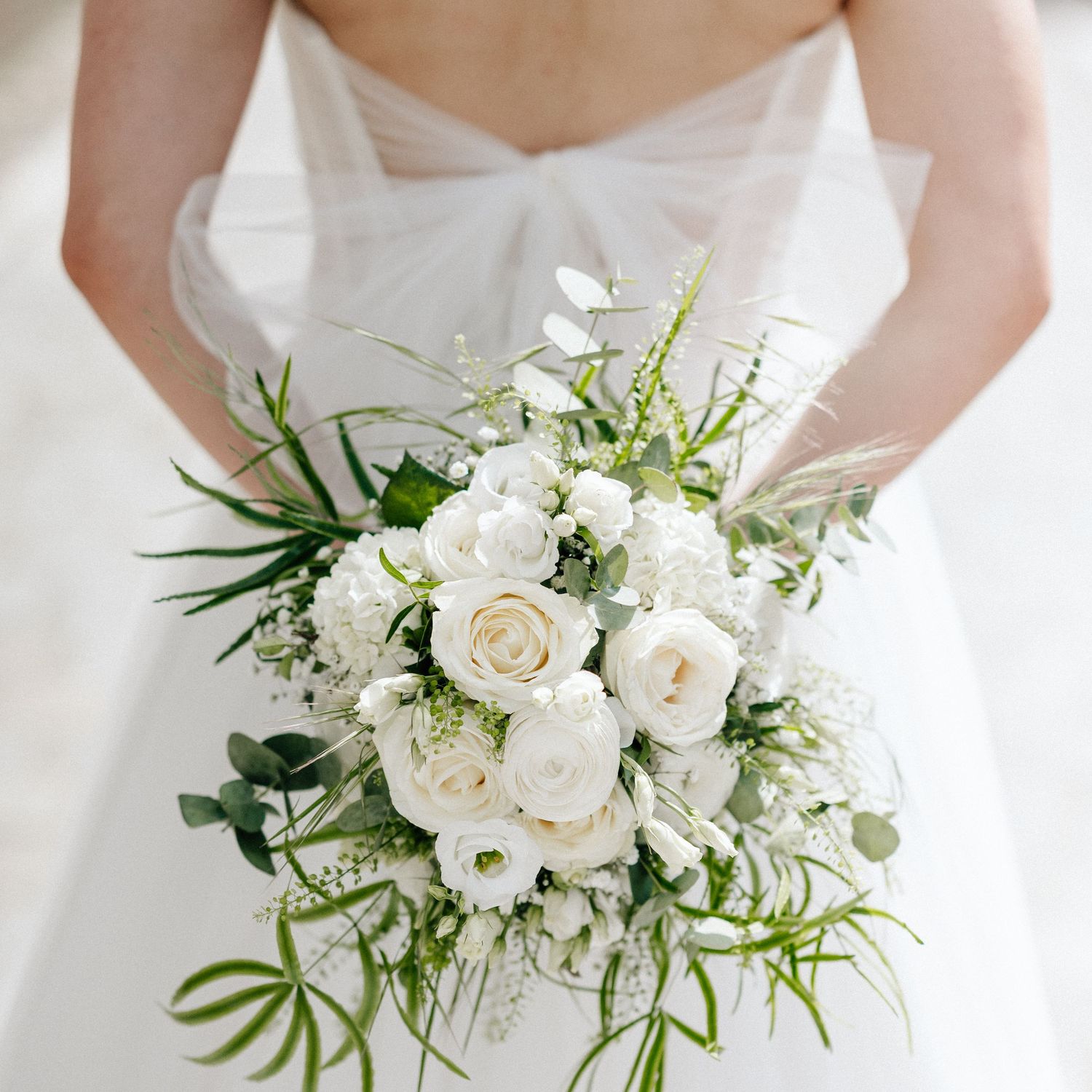 A collection of elegant white bridal bouquets with roses and delicate greenery arranged in a row.