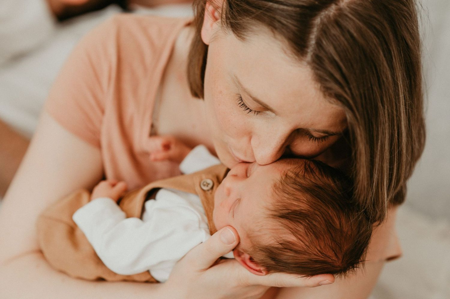 Gentle intimate moment between adult and sleeping newborn in soft lighting.