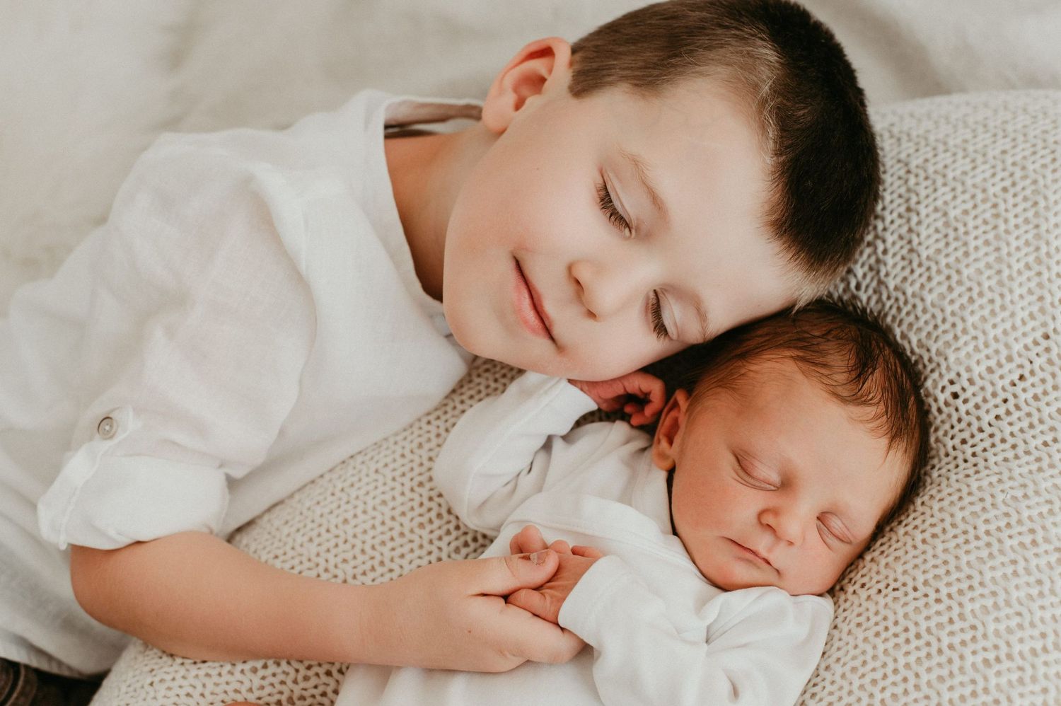 Two siblings sharing peaceful sleeping moment on white textured blanket.