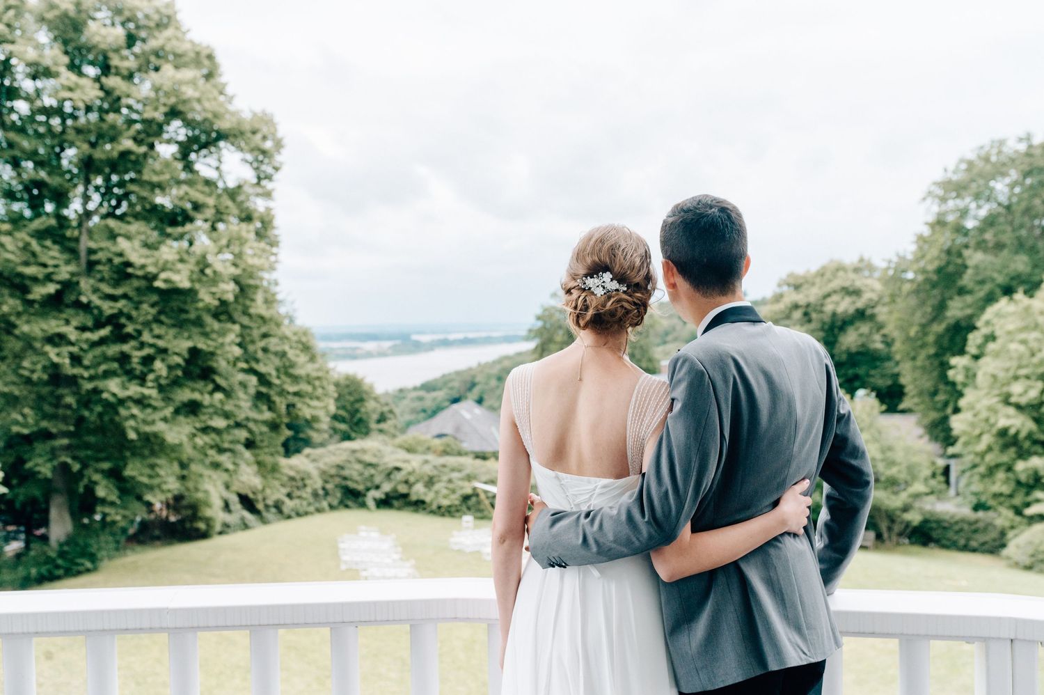 Romantic couple overlooking scenic view from balcony in elegant wedding attire.