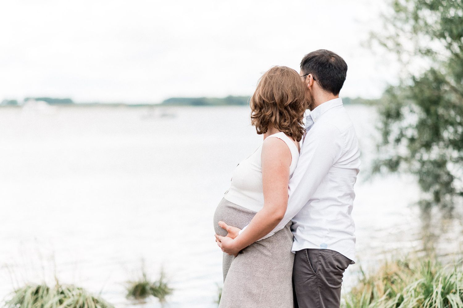 Romantic silhouettes of a couple embracing near a waterfront with trees in the background.