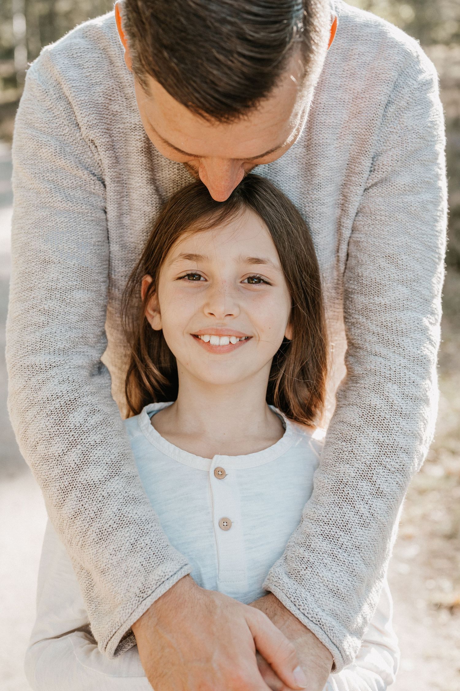 A tender moment captured outdoors showing a parent in a gray sweater embracing their child wearing a white top.