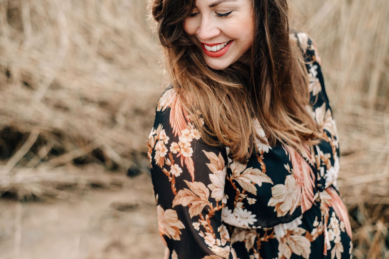 Woman in floral dress poses during outdoor autumn photoshoot with warm natural lighting.