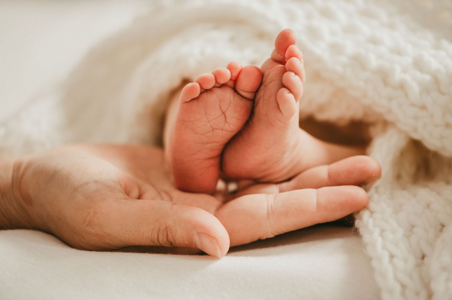 Close-up of newborn baby feet on textured cream blanket.