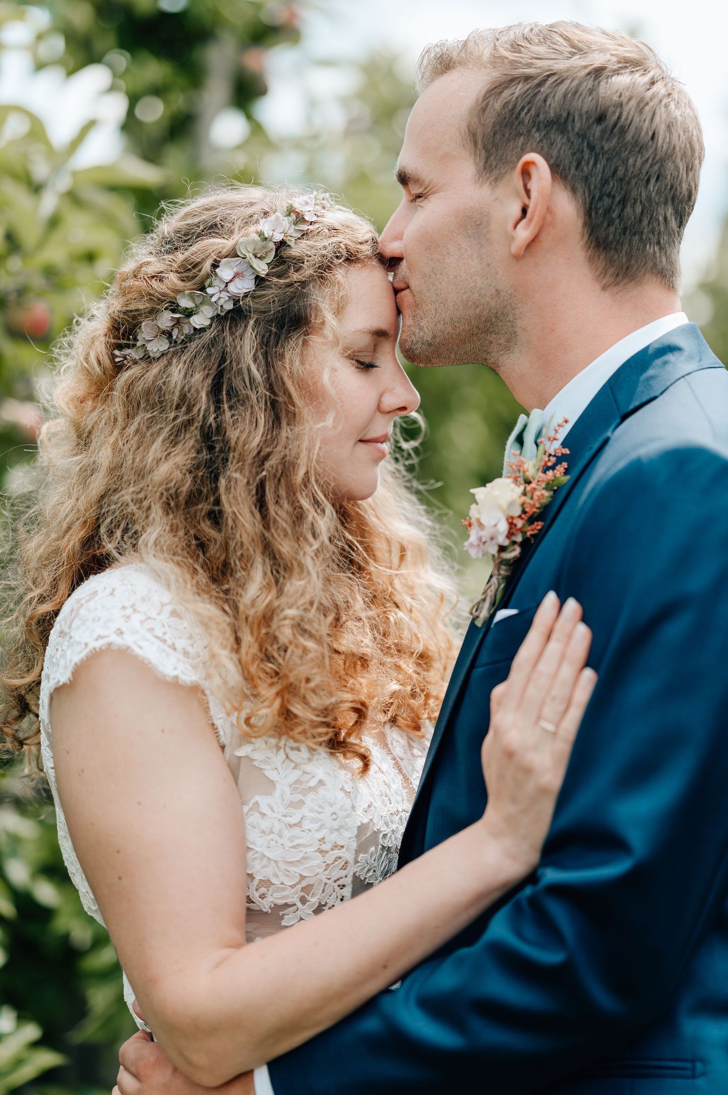 Intimate wedding portrait of couple sharing a tender moment among garden foliage.