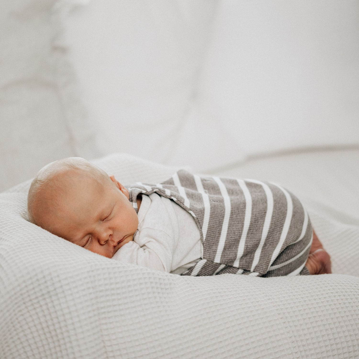 A peaceful sleeping newborn wrapped in striped and white swaddle blankets rests on soft bedding.