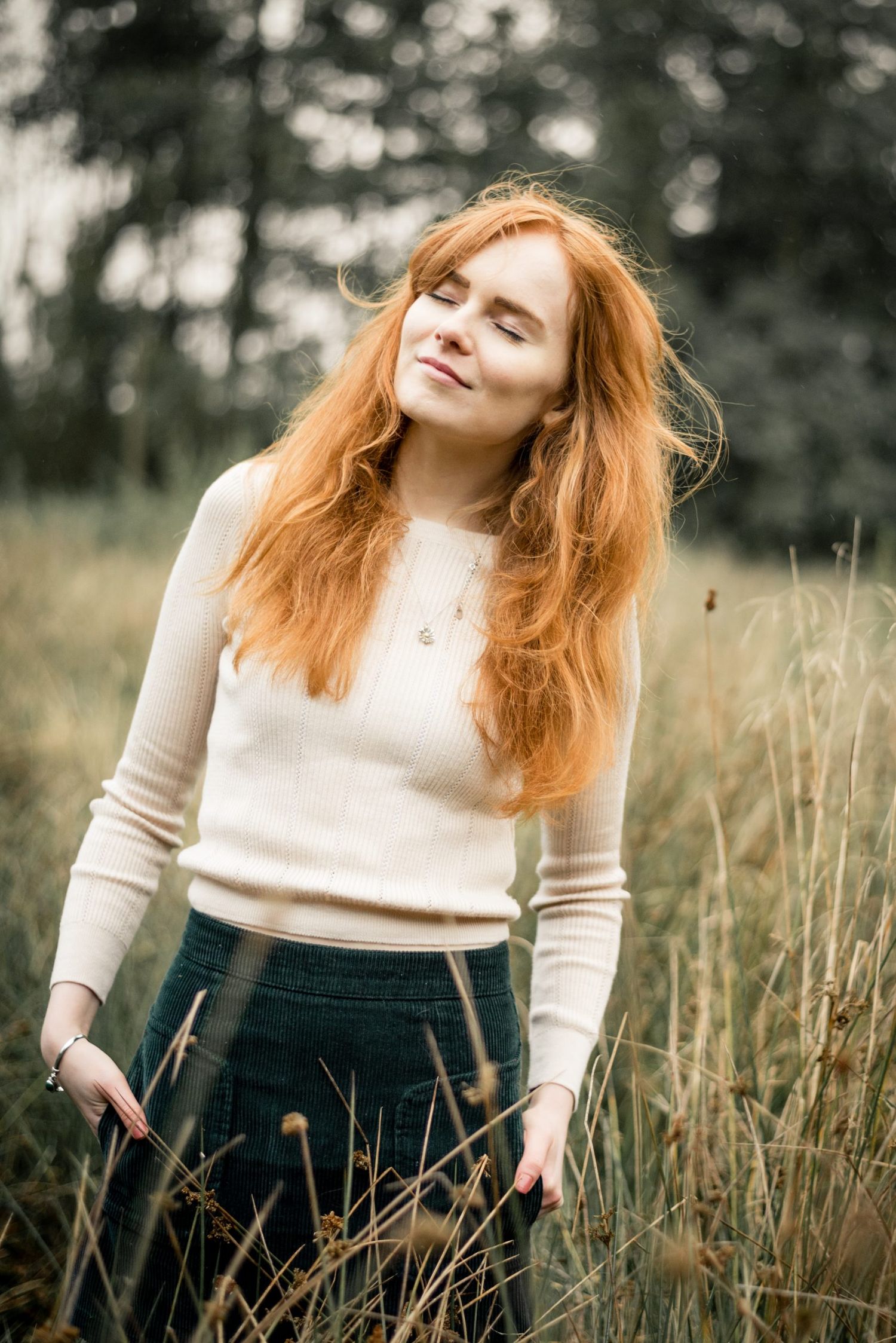 Outdoor portrait session in tall grass featuring cream sweater and natural autumn lighting.