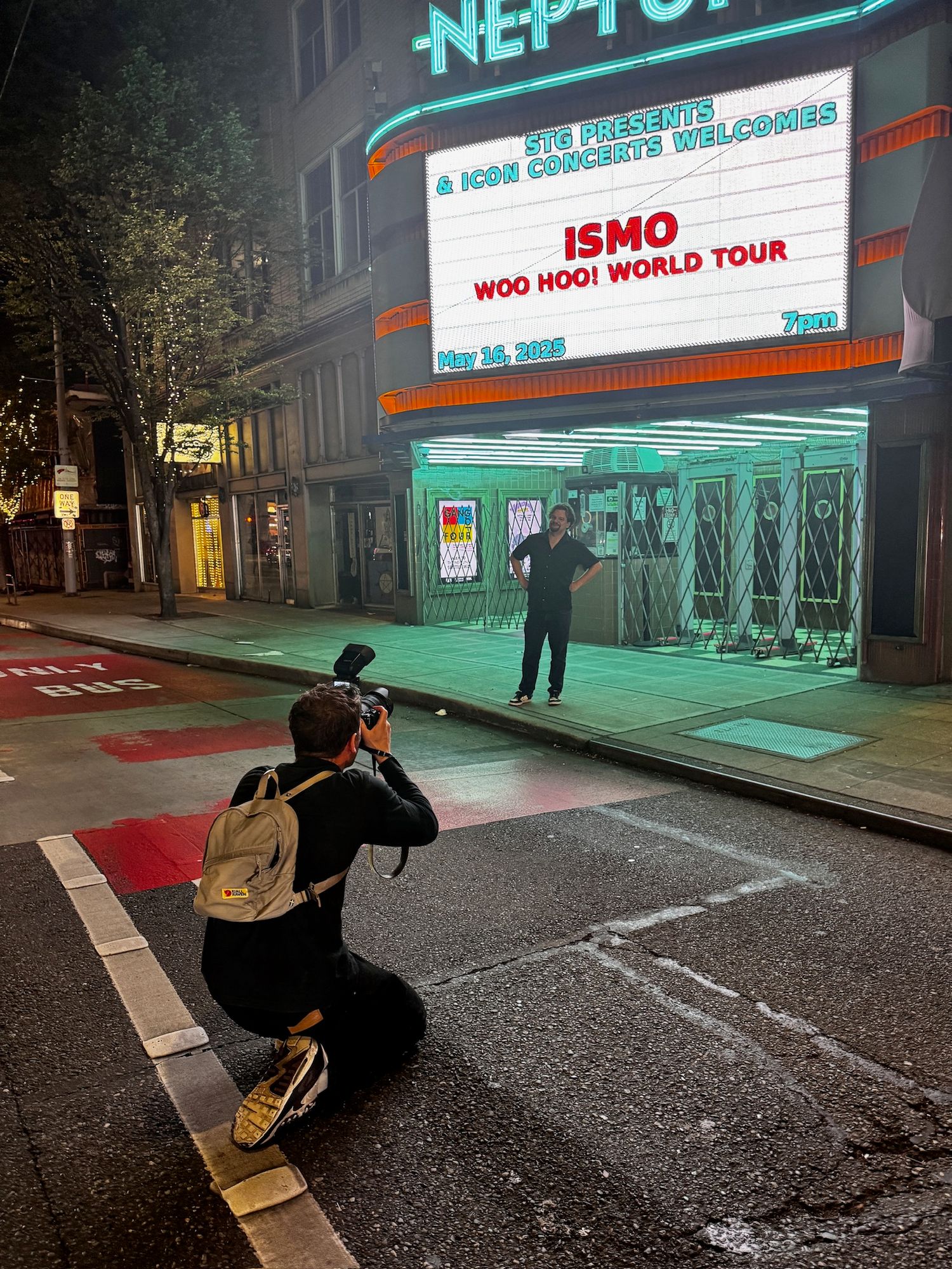 Photographer crouches to capture comedian ISMO outside Neptune Theatre on Woo Hoo World Tour.