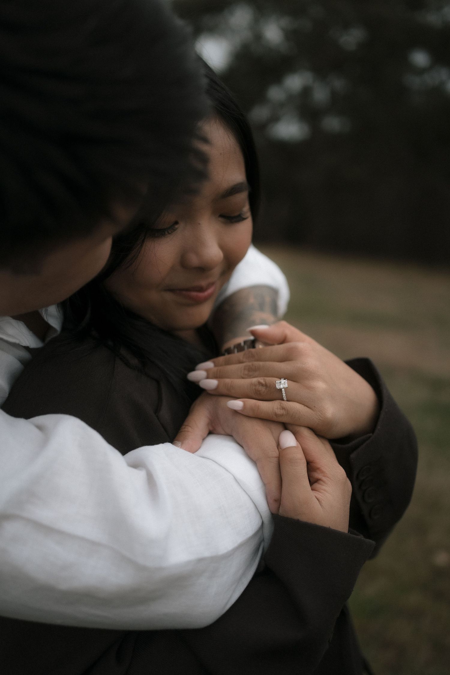 A couple shares an intimate moment outdoors as an engagement ring sparkles in the sunlight.